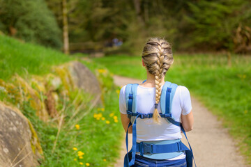 Back view of a blonde woman walking through a park with her little baby