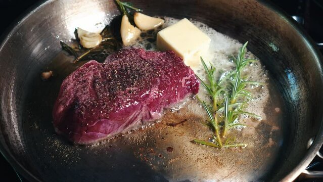 Searing steak in a skillet with herbs 