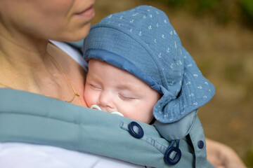 Close up of a baby sleeping in a baby carrier on his mother's chest