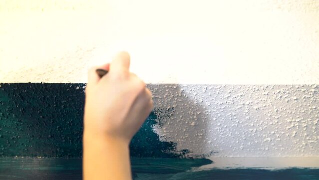 painting a white wall with blue paint and a small brush