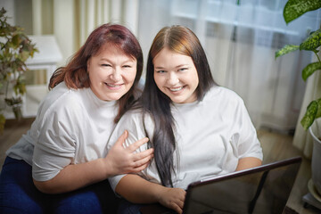 Fat funny funny adult mother and daughter with laptop indoors. A teenage girl teaches middle-aged woman modern technology. Internet, chatting