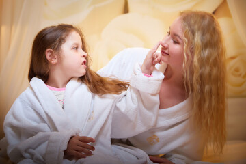 Mother and daughter happily relax and fun together on a bed in bedroom. The concept of tenderness between mom and girl