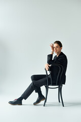 A stylish young man in a suit sits on a chair, exuding confidence and contemplation in a studio...