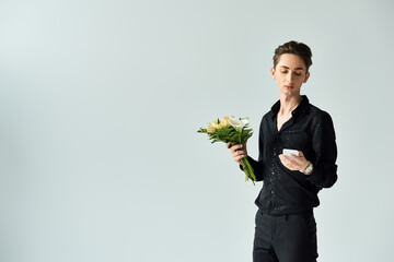A young queer person holding a bouquet of flowers in a studio setting on a grey background.