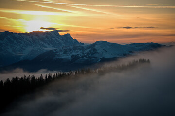 orange sunrise in the austrian alps, the golden hour at a spring morning, with beautiful view of cloudy and foggy mountains