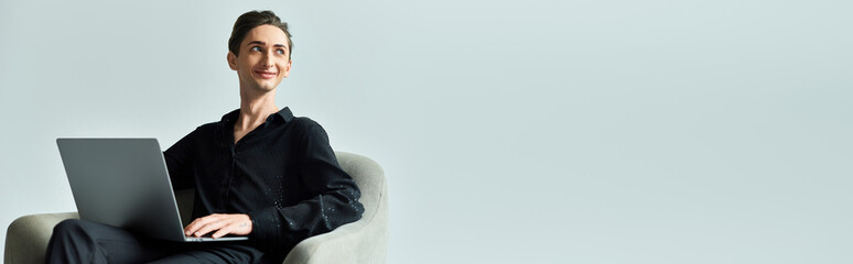 A young queer person sits in a chair with a laptop in a studio, showcasing LGBTQ pride and creativity.