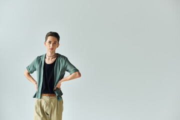 A young queer person strikes a pose in front of a white background, exuding confidence and pride as...