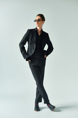 Young queer man in a stylish black suit striking a confident and proud pose against a grey...