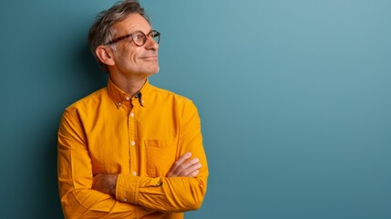 Fototapeta premium A man in a yellow shirt and glasses stands with crossed arms before a blue backdrop