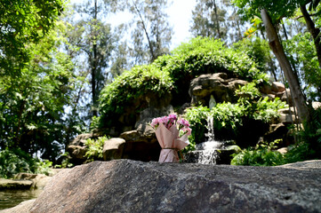 Closeup of A bouquet of pink flowers placed on the rocks in front of The Cave Our lady of grace virgin Mary with natural background in Waterfall flows down from the rock cave at Thailand.