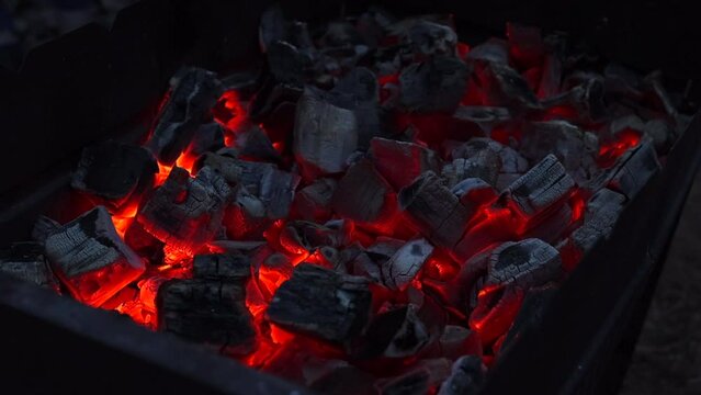 Burning red organic charcoal texture in bbq grill in the dark at night. Bonfire outdoor. Barbecue process in slow motion. Coal and fire texture