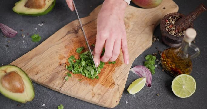 Woman cutting and chopping cilantro or parsley greens on a wooden cutting board at domestic kitchen