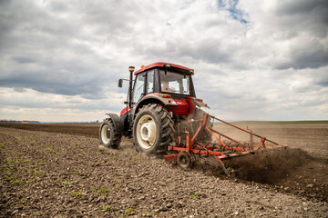 Powerful red tractor tills the soil on a vast farm with a dramatic cloudy sky overhead