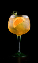 glass of tropical gin cocktail with orange and rosemary isolated on black background