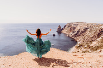 Woman green dress sea. Female dancer posing on a rocky outcrop high above the sea. Girl on the nature on blue sky background. Fashion photo.