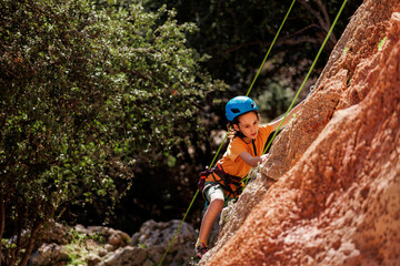 Obraz premium child is rock climbing at a summer camp. rock climber boy. sport in nature. cute teenager climbs a rock with a belay. active holidays.