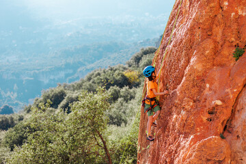 sport in summer camp. a child is rock climbing at a summer camp. rock climber boy. sport in nature on a sunny day. cute teenager climbs a rock with a belay. active holidays.