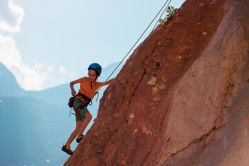sport in summer camp. a child is rock climbing at a summer camp. rock climber boy. sport in nature on a sunny day. cute teenager climbs a rock with a belay. active holidays.