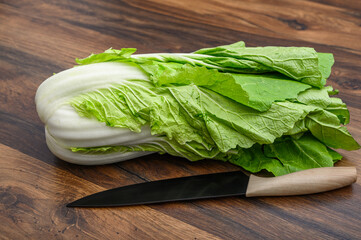 Cała zielona kapusta właściwa pekińska leży na blacie w kuchni, obok nóż kuchenny do szatkowania 