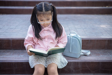 Cute little asian girl sitting on the stairs reading a book