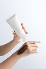 Creative design template for advertise scrub which has manufactured from natural ingredient like coffee, a blank label cosmetic tube held by a hand, a coffee smudge. Copy space, front view