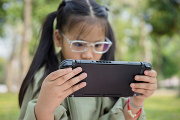 Girl playing video game with handheld game console at garden