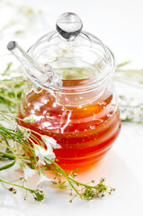 Honey in a glass jar and dipper over white background. Healthy organic honey with glass spoon in transparent glass jar. Wild flowers, healthy honey close up.