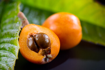 Loquat fruit or Japanese medlars, Nispero, Eriobotrya japonica with leaves fresh ripe bio vegetarian food, medlar berries. Close up. On black background table. 