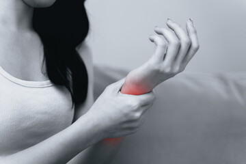 Closeup of woman sitting on sofa holds her wrist, hand injury with red highlight