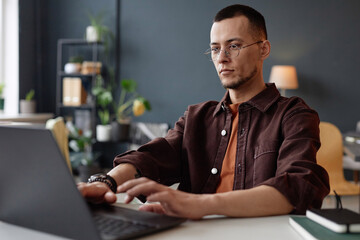 Portrait of young Asian man wearing glasses and using laptop in office with serious face expression