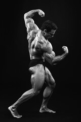 Athlete bodybuilder posing for a sports magazine in the studio on a black background. Grain effect used