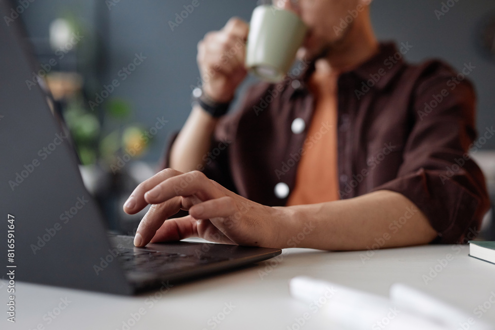 Aufkleber close up of unrecognizable man typing at laptop keyboard while working at desk and drinking coffee c