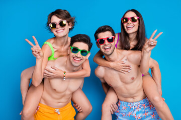 Photo of good mood friendly fellows company wear swimsuits having fun showing v-signs isolated blue...