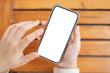 Top view image of a woman's hand holding a white-screen smartphone mockup over a wooden table.