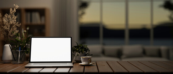 A white screen laptop computer mockup on a wooden table in a modern dark living room.
