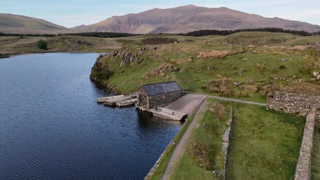 Aerial drone reveal shot of the boathouse at Llyn Dywarchen with Yr Wyddfa in the background.