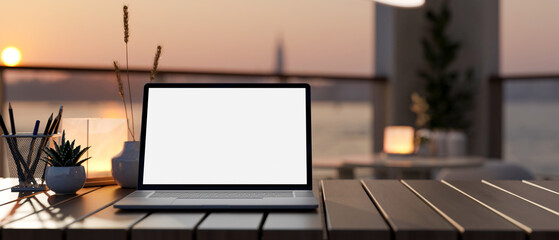A laptop computer mockup on a wooden table with a blurred background of a river at sunset.