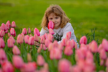 Kid in spring tulips blossom park. Happy childhood. Spring holidays. Adorable kid smelling tulips in spring garden. Cute little kid boy in a blossom flowering nature. Portrait of kid in spring garden.