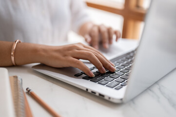 A close-up image of a woman typing on keyboard, working on the computer at a table in a coffee shop.