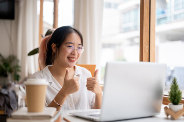 A woman is having an online meeting with her team via her laptop computer, showing her thumbs up.