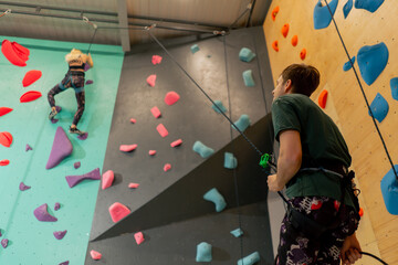 at the climbing wall young girl climbs the wall for the first time, the coach belays with a safety...
