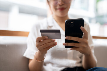 A cropped image of a woman holding a credit card and her smartphone on a sofa in the living room.