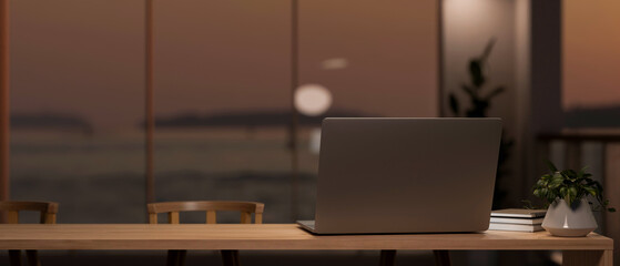 A laptop on a table in a modern room with an amazing large glass window with an ocean view at sunset