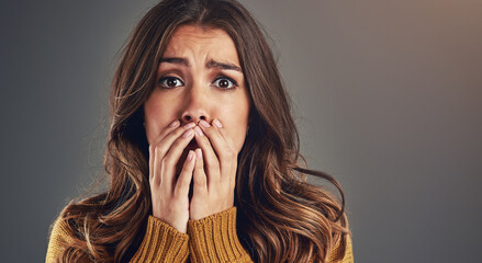 Portrait, scared and woman with fear, surprise and emotions with secret news on grey studio background. Face, person and model with reaction, shocked and cover mouth with anxiety and emoji of gossip