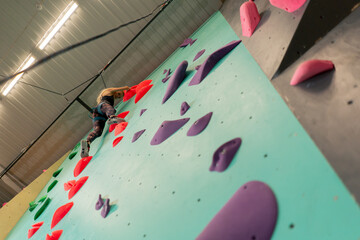 at the climbing wall young girl climbs the wall for the first time, the coach belays with a safety...