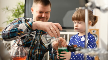 Man and little girl play with colourful liquids portrait. Young team clean research equipment...