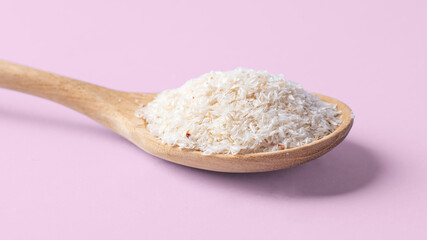 Psyllium husk in wooden spoon, closeup on pink background