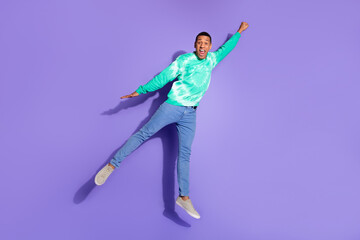 Full length photo of excited funny guy wear teal sweatshirt jumping high emtpy space isolated purple color background