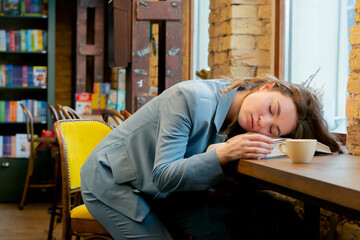 in bookstore near the window a beautiful sleepy student is sitting reading books preparing for exams