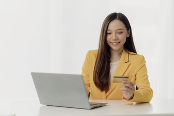 Attractive Asian woman holds smartphone and credit card on her laptop using mobile banking or...